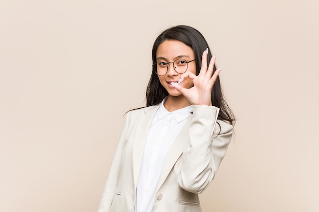 Mujer china joven del negocio alegre y confiada que muestra gesto aceptable.