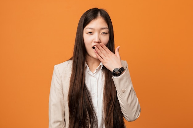 Mujer china joven del negocio que bosteza mostrando un gesto cansado que cubre la boca con la mano.