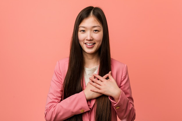 La mujer china joven del negocio que lleva el traje rosado tiene expresión amistosa, presionando la palma al pecho. Concepto de amor