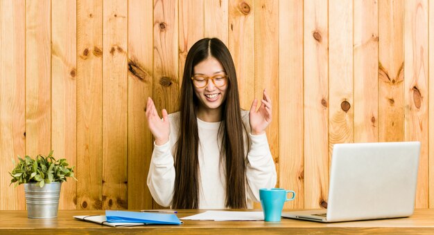 Mujer china joven que estudia en su escritorio alegre riendo mucho. Concepto de felicidad