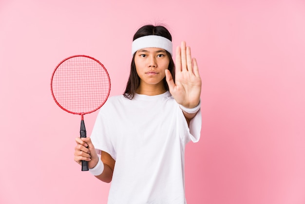 Mujer china joven que juega a bádminton en una pared rosada que se coloca con la mano extendida que muestra la señal de stop, previniéndole.