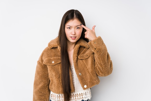 Mujer china joven que presenta en una pared blanca aislada mostrando un gesto de decepción con el índice.