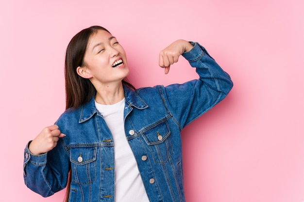 La mujer china joven que presentaba en un fondo rosado aisló levantar el puño después de una victoria, concepto del ganador.