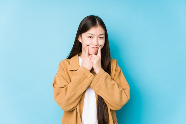 La mujer china joven que presentaba en una pared azul aisló dudar entre dos opciones.