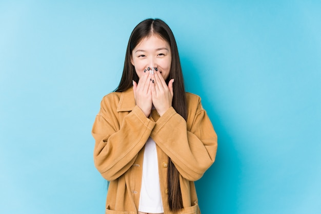 La mujer china joven que presentaba en una pared azul aisló reír sobre algo, cubriendo la boca con las manos.