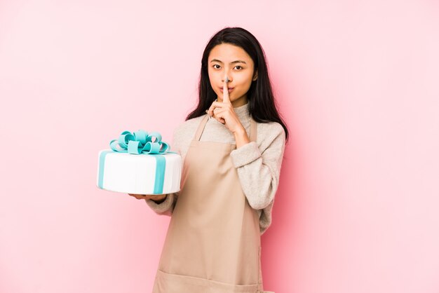 Mujer china joven que sostiene una torta aislada mostrando el número dos con los dedos.