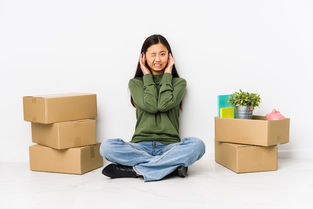 Mujer china joven que se traslada a un nuevo hogar que cubre los oídos con las manos.