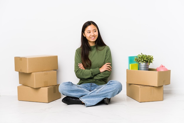 Mujer china joven que se traslada a un nuevo hogar que sonríe confiado con los brazos cruzados.