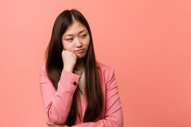 Mujer china del negocio joven que lleva el traje rosado que siente triste y pensativo, mirando el espacio de la copia.