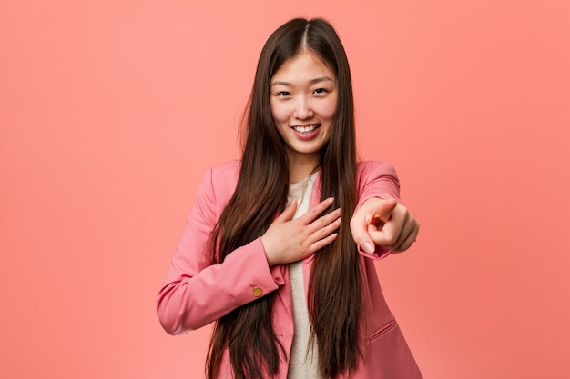 La mujer china del negocio joven que lleva el traje rosado señala con el dedo pulgar lejos, riendo y despreocupado.