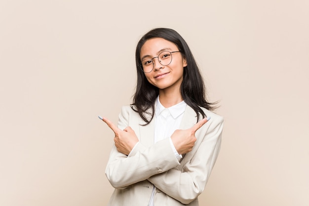 La mujer china de negocios joven apunta hacia los lados, está tratando de elegir entre dos opciones.