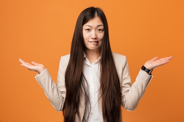 Mujer china de negocios joven confundida y dudosa levantándole las manos para sostener un espacio de copia.