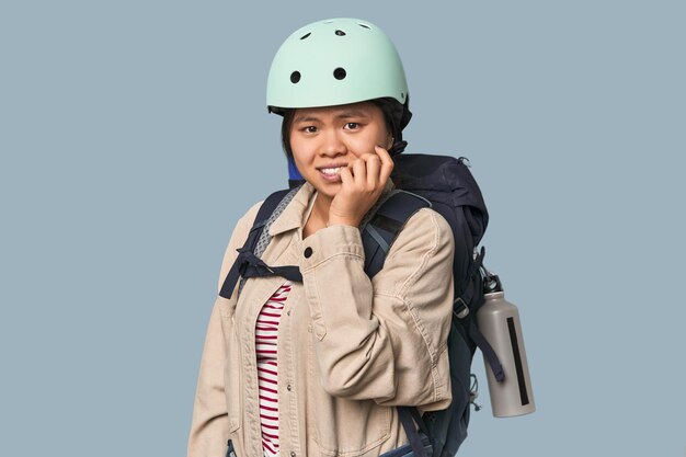 Mujer china preparada para actividades de montaña mordiendo las uñas nerviosa y muy ansiosa