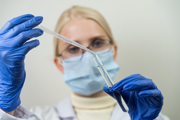 Mujer científica con un frasco de vidrio y una pipeta en las manos. Un asistente de laboratorio gotea un líquido transparente en un matraz con una preparación especial. Experimento científico.