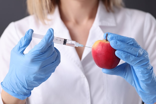 Mujer científica en guantes de goma haciendo inyección en primer plano de la manzana. Ingeniería genética