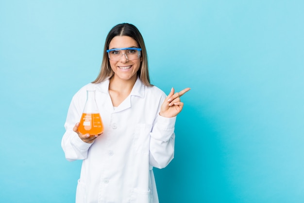 Mujer científica joven que sonríe y que señala a un lado, mostrando algo en el espacio en blanco.