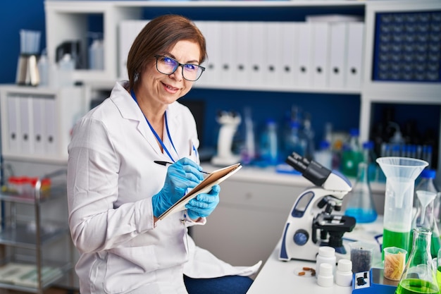 Mujer científica de mediana edad escribiendo en un cuaderno en el laboratorio