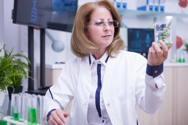 Mujer científica de mediana edad sosteniendo una muestra de planta verde en un tubo de ensayo. Laboratorio de investigación.