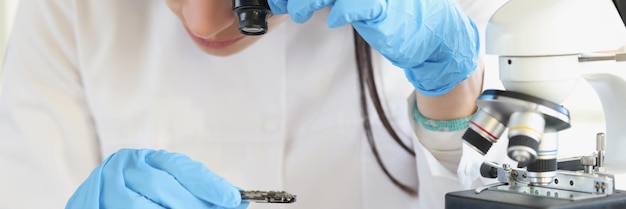 Mujer científica mirando a través de una lupa al chip de la computadora cerca del microscopio en el laboratorio