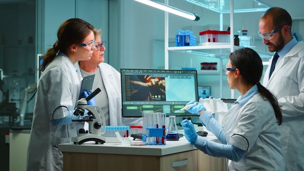 Mujer científica pipeteando líquido al tubo de ensayo que trabaja en el laboratorio equipado a altas horas de la noche. Químicos que examinan la evolución del virus utilizando alta tecnología para el análisis científico del desarrollo de tratamientos contra covid19