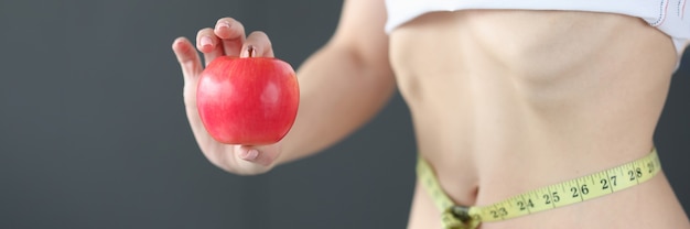 Mujer con cinta métrica en la cintura sosteniendo la manzana en las manos concepto de comida de dieta de primer plano