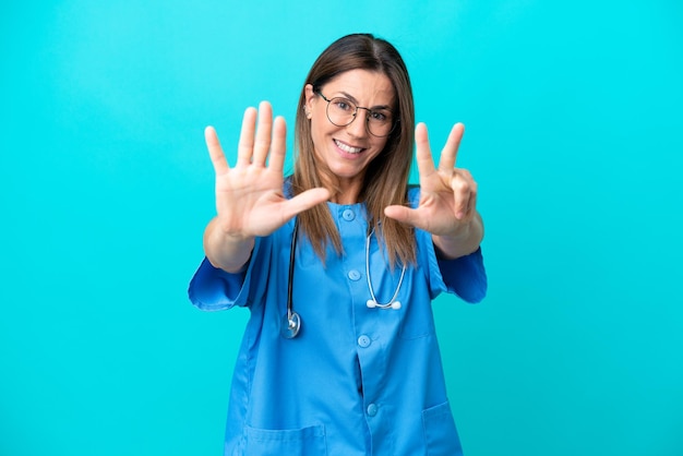 Mujer cirujana de mediana edad aislada de fondo azul contando ocho con los dedos