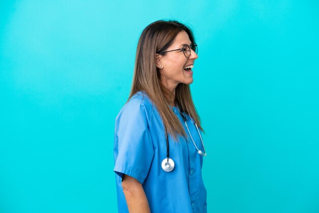 Mujer cirujana de mediana edad aislada de fondo azul riéndose en posición lateral