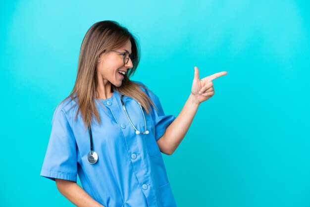Foto mujer cirujana de mediana edad aislada de fondo azul señalando con el dedo al lado y presentando un producto