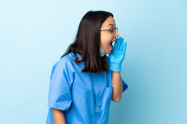 Mujer de cirujano sobre pared azul aislado gritando con la boca abierta a un lado