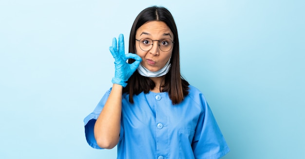 Mujer cirujano sobre pared azul que muestra un signo de gesto de silencio