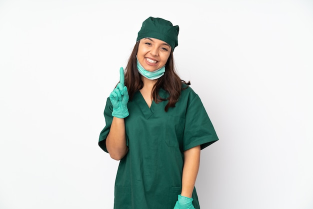 Mujer de cirujano en uniforme verde en la pared blanca mostrando y levantando un dedo en señal de lo mejor