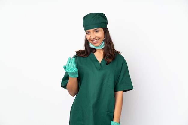 Mujer de cirujano en uniforme verde sobre blanco invitando a venir con la mano. Feliz de que hayas venido