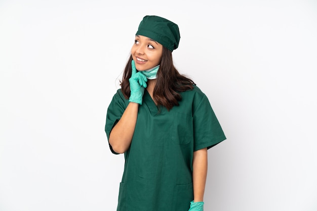 Mujer de cirujano en uniforme verde sobre blanco pensando una idea mientras mira hacia arriba