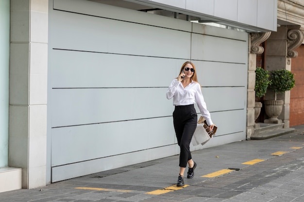 Mujer en la ciudad haciendo compras de ganga llevando sus maletas mientras habla por teléfono