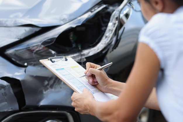 Una mujer en un coche averiado llena un documento de primer plano borroso accidente de carretera daños por colisión