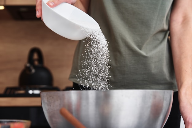 Mujer en la cocina cocinando una masa. Manos vierten harina en un bol