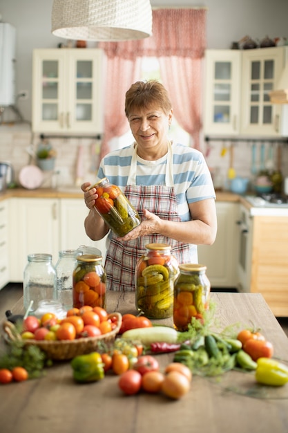 Mujer en la cocina hace encurtidos de tomates y pepinos, Mujer en la cocina enlatado de verduras