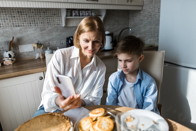 mujer en la cocina en la mesa con el niño está mirando el teléfono.