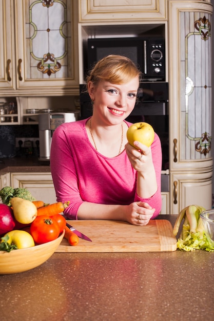 La mujer en la cocina se prepara una cena y come una manzana. Concepto de alimentación saludable