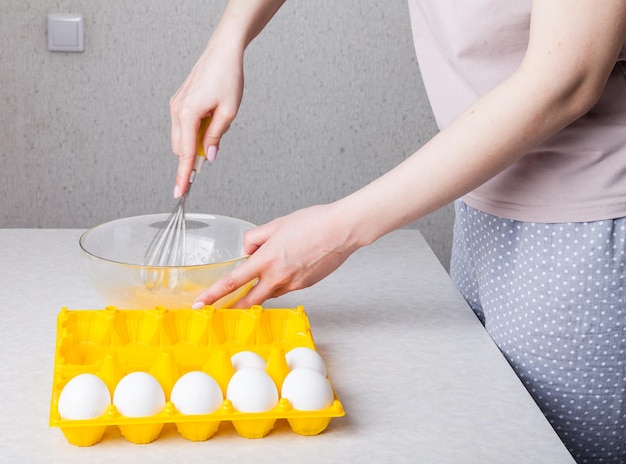 Foto una mujer en la cocina sostiene un batidor en sus manos con un mango amarillo y los bate con huevos en un recipiente de vidrio transparente la rutina diaria de la madre prepara el desayuno de huevos fritos para la familia