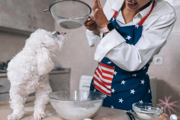 La mujer en la cocina tamiza la harina junto con un perro