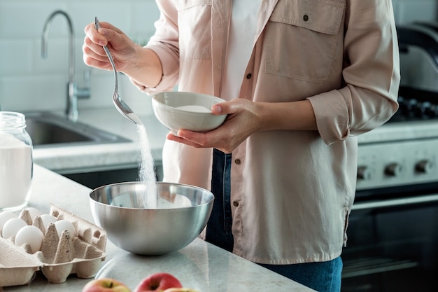 Una mujer en la cocina vierte azúcar granulada de un bol. Cocinando.