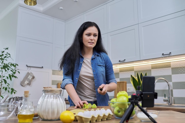 Mujer cocinando en casa en la cocina hablando en línea usando una videollamada en un teléfono inteligente