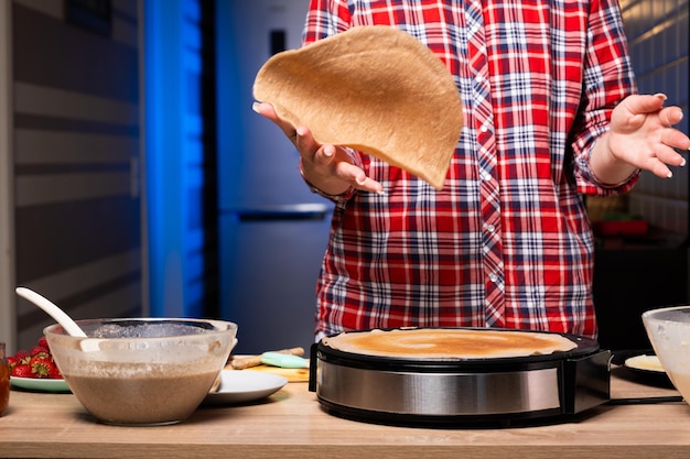 Mujer cocinando deliciosas crepes en la máquina de panqueques eléctrica en el primer plano de la cocina