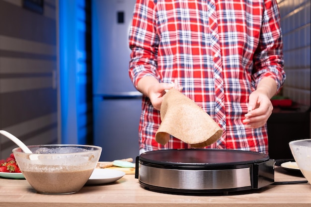 Foto mujer cocinando deliciosos crepes en una máquina eléctrica para hacer panqueques en el primer plano de la cocina