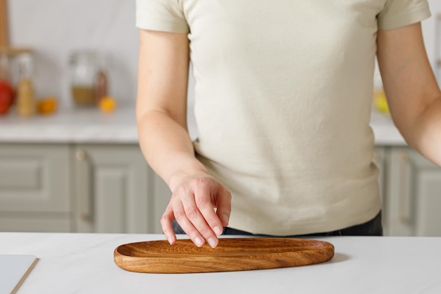 Mujer cocinando en la encimera de la cocina lista para cocinar usando una bandeja de tablero de roble ovalada de madera vacía