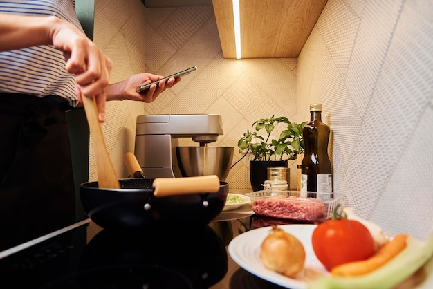 Mujer cocinando salsa boloñesa y uso smartphone