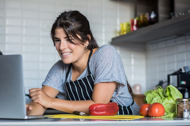 Foto mujer cocinando y siguiendo receta en laptop pc