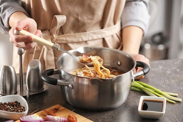 Mujer cocinando sopa de fideos de pollo en la mesa de la cocina