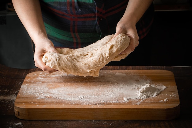 Mujer cocinera amasa harina en el tablero de masa de pizza elástica manos primer plano